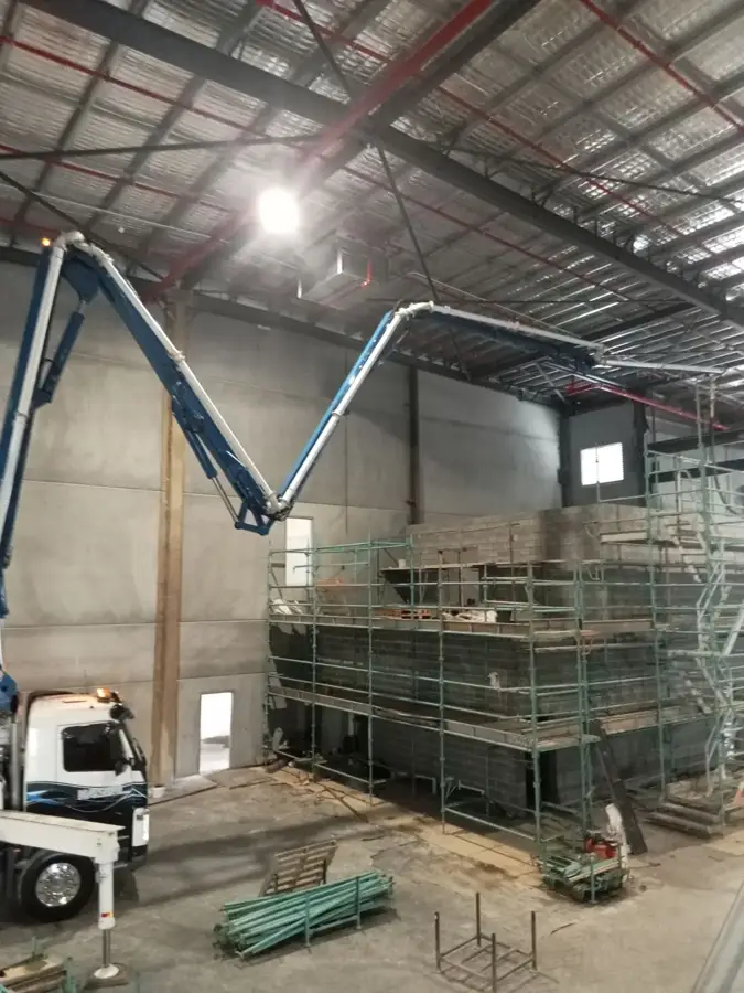 Concrete boom pump reaching inside a factory warehouse to place concrete for an internal pour
