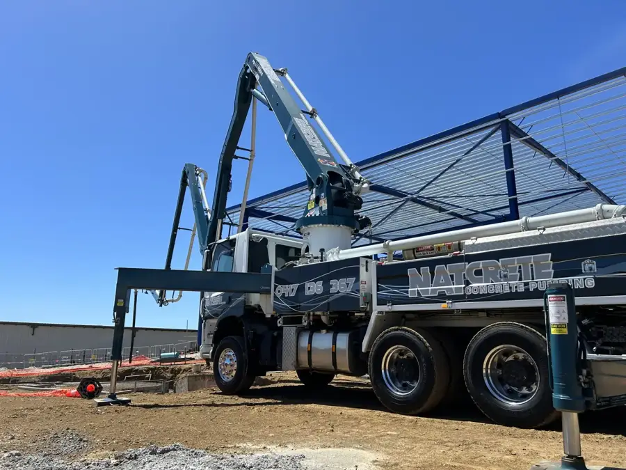 Natcrete boom pump with outriggers down and boom raised beside a steel-framed building site